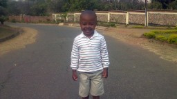 A small boy, Ethan, stands in a road smiling to camera.