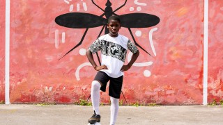 Boy in front of large image of mosquito, steadies a football under his foot