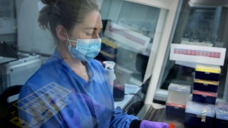 A scientist working in a lab wearing blue overalls.